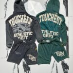 Dark gray and forest green athletic hoodie and shorts sets with vintage 'TOUGHEDY ATHLETIC DEPT' graphics, displayed on a marbled background.