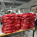 Stack of freshly manufactured red varsity jackets with white and red striped detailing, piled on a table in Ansons Apparel factory.